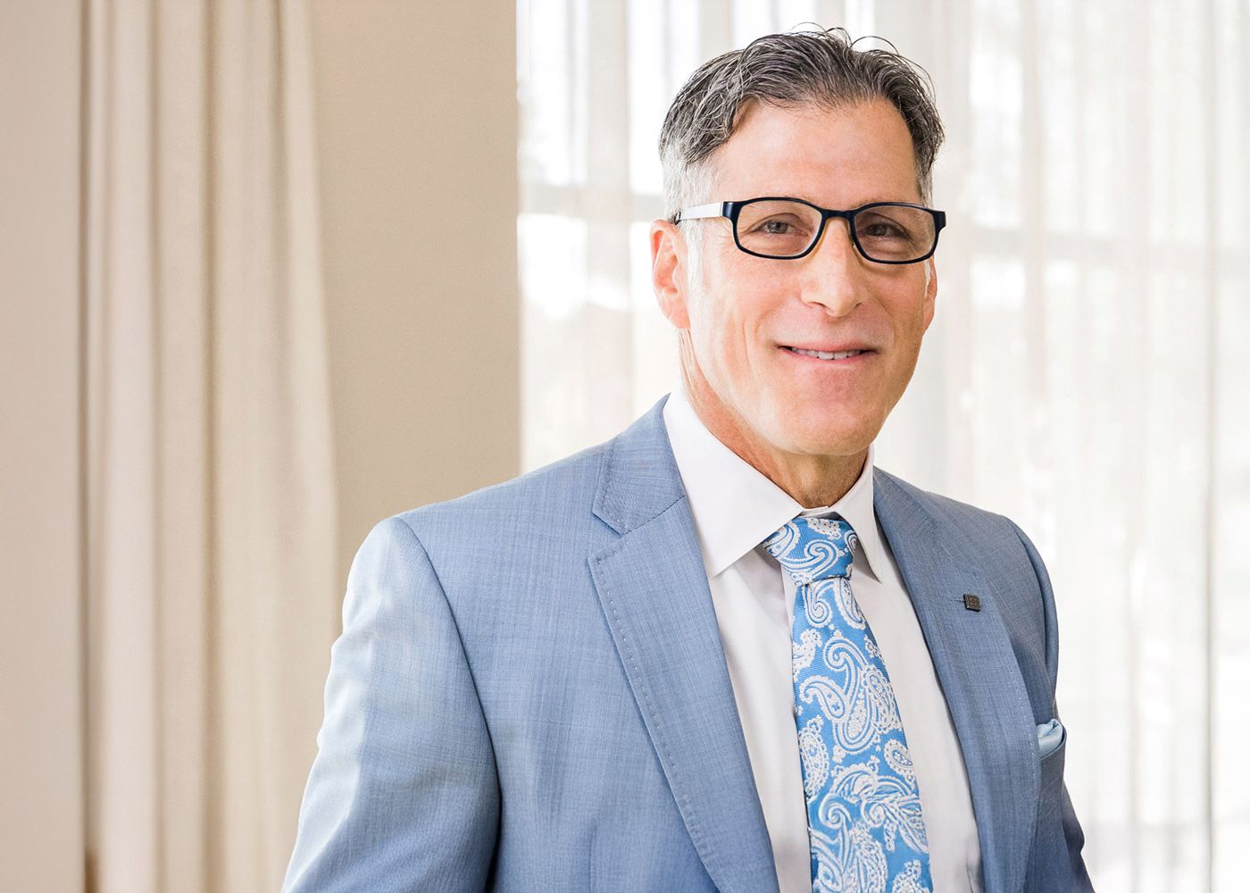 Smiling man in blue suit and patterned tie.