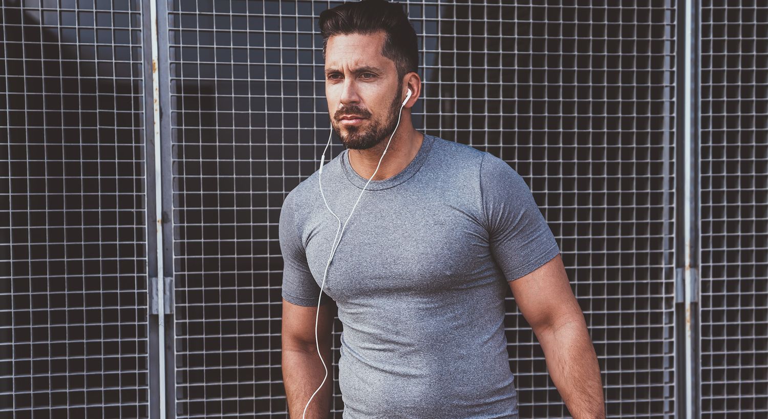 Man in gray shirt listening to music outdoors.