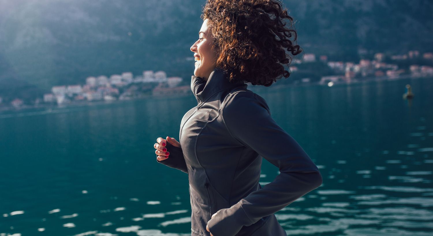 Woman jogging by the water with mountains in background.