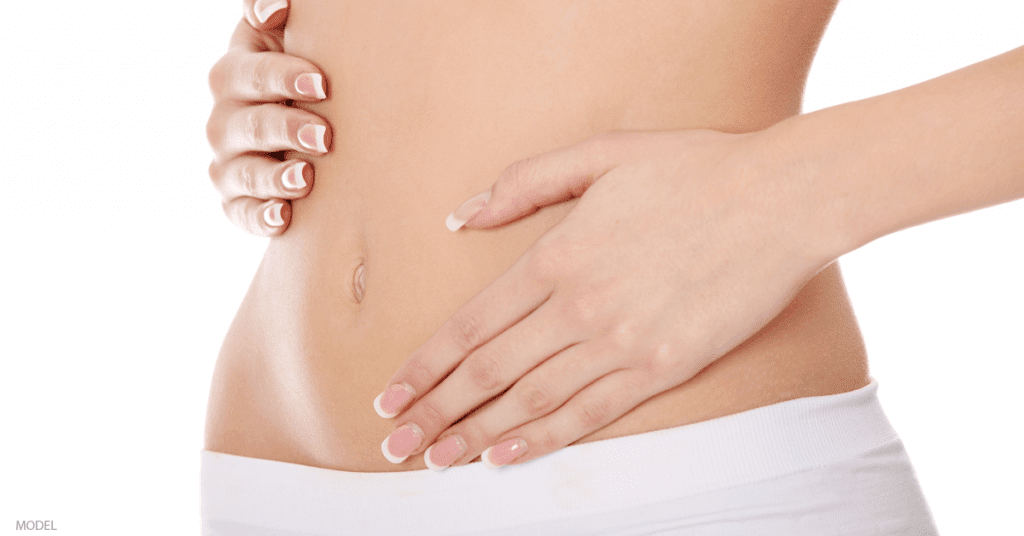 A woman touches her stomach following her mommy makeover.