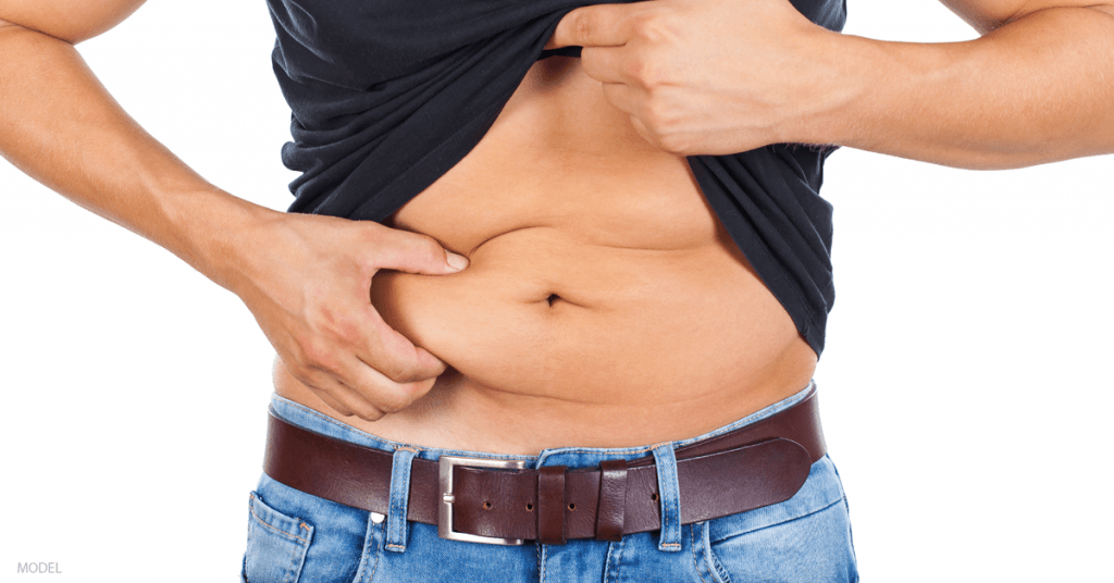 A man considering liposuction pinches a section of skin on his stomach.